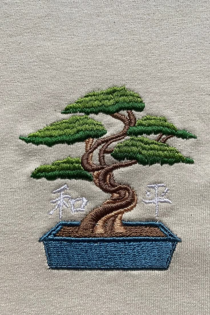 Kunstvoller Bonsai-Baum mit japanischen Schriftzeichen, gestickt auf hellem Stoff